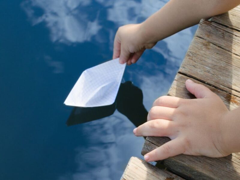 Hands gently placing a paper boat on calm water, symbolizing choosing to give your worries to God and leave them safely in His hands.