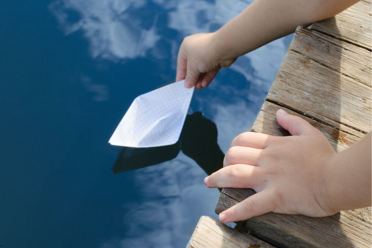 Hands gently placing a paper boat on calm water, symbolizing choosing to give your worries to God and leave them safely in His hands.
