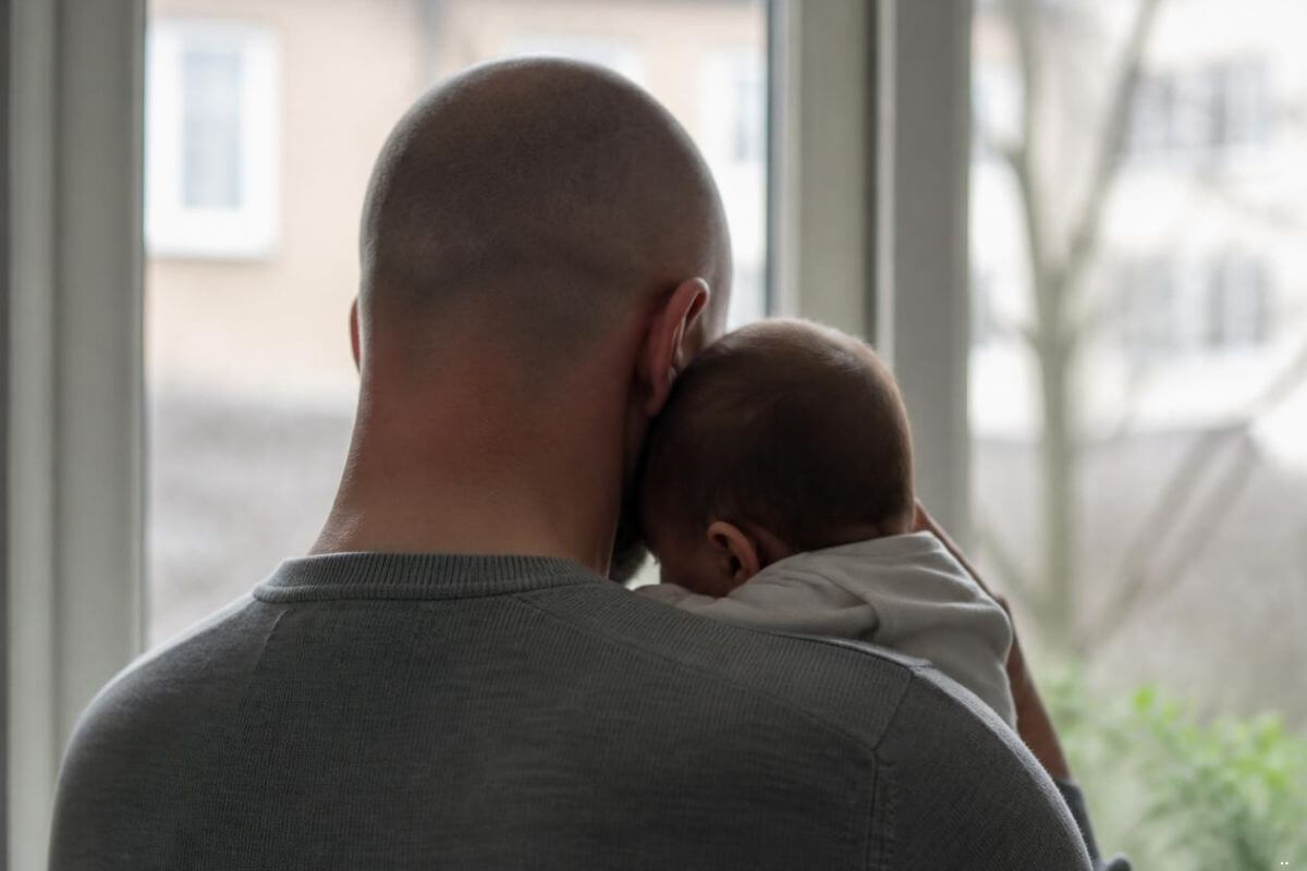 Father gently holding a sleeping baby, illustrating the loving protection of a parent who knows what a child is ready to carry.