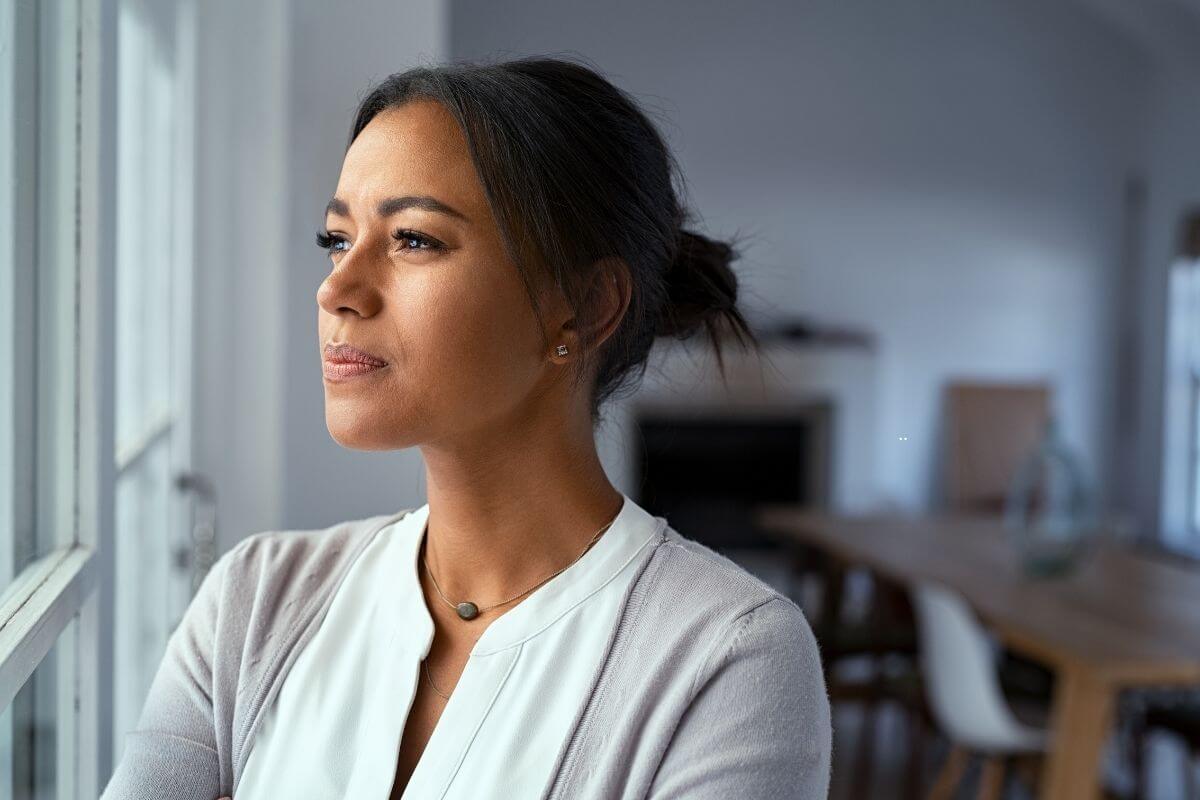 Woman looking thoughtfully through a window, reflecting on what lies ahead.