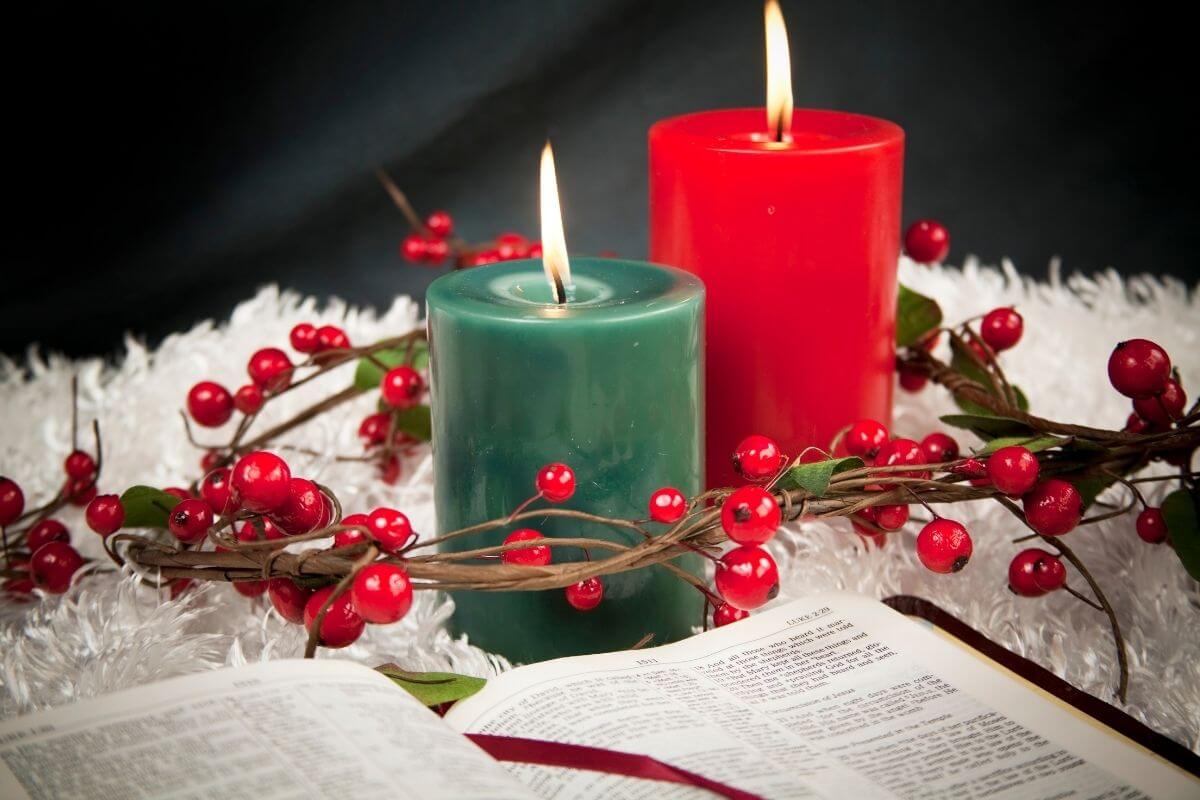 Two lit candles—one red and one green—surrounded by a wreath of red berries and green leaves, resting on a white textured surface beside an open Bible showing Luke 2:10. A peaceful Christmas scene symbolizing faith and reflection, perfect for posts about Christmas scriptures for hope and peace.