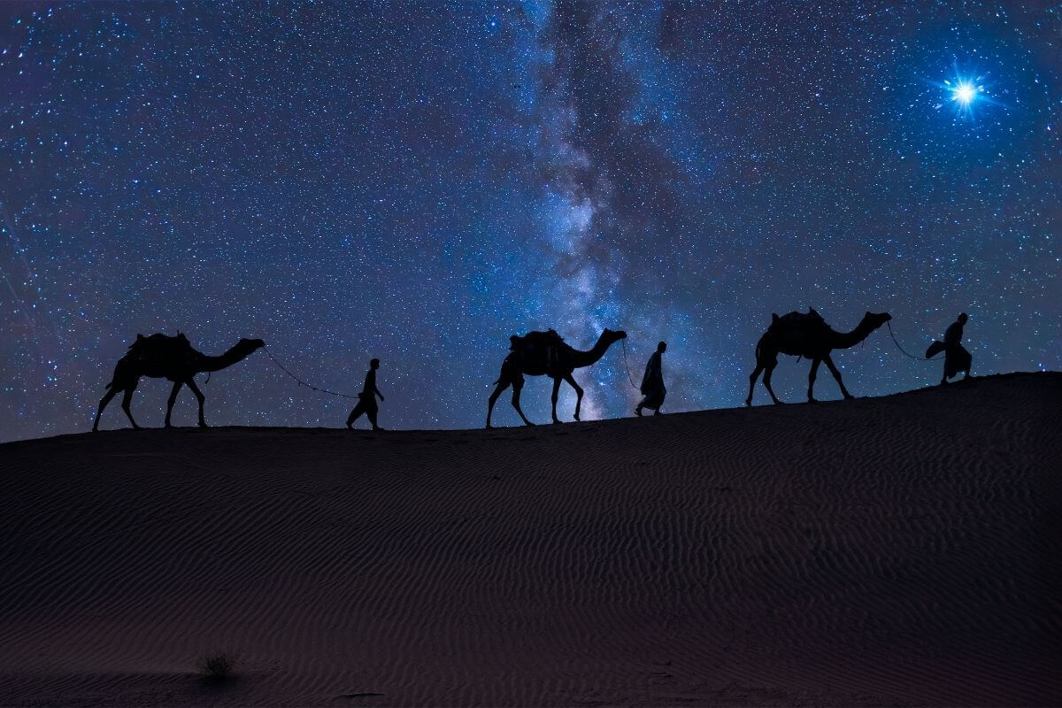 Star on the sky with three camels and wisemen walking in a dark starry night to see the born King Jesus in Bethlehem.