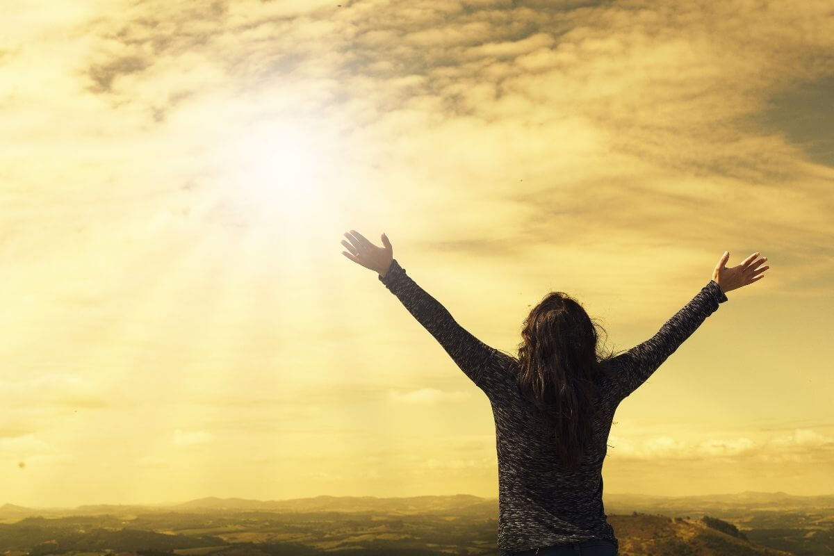 Woman at sunrise with hands lifted in rejoicing and worship to God.